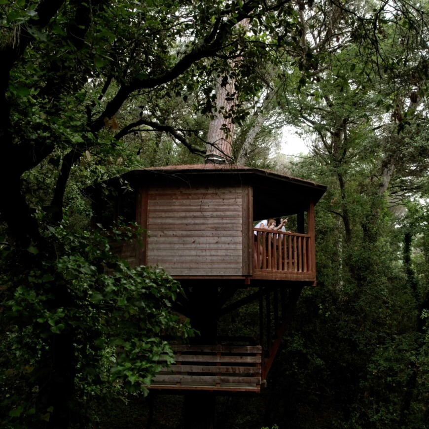 Gent a una cabanya de fusta singular d'alt d'un arbre senyalant al cel en un lloc a la natura amb molt encant